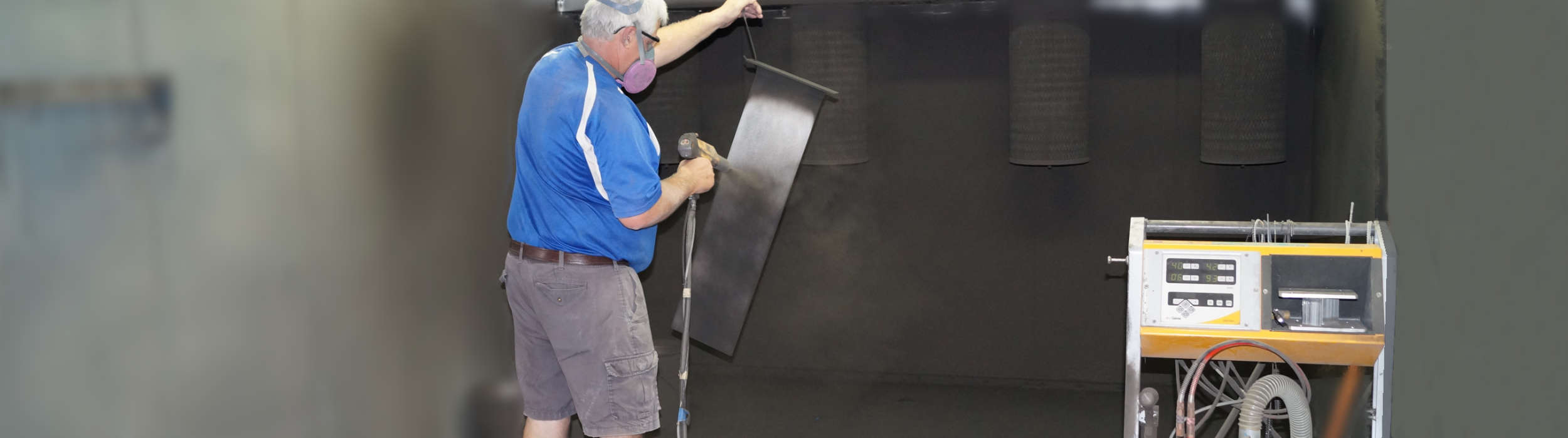 Worker spraying a sign panel inside the powder-coat booth